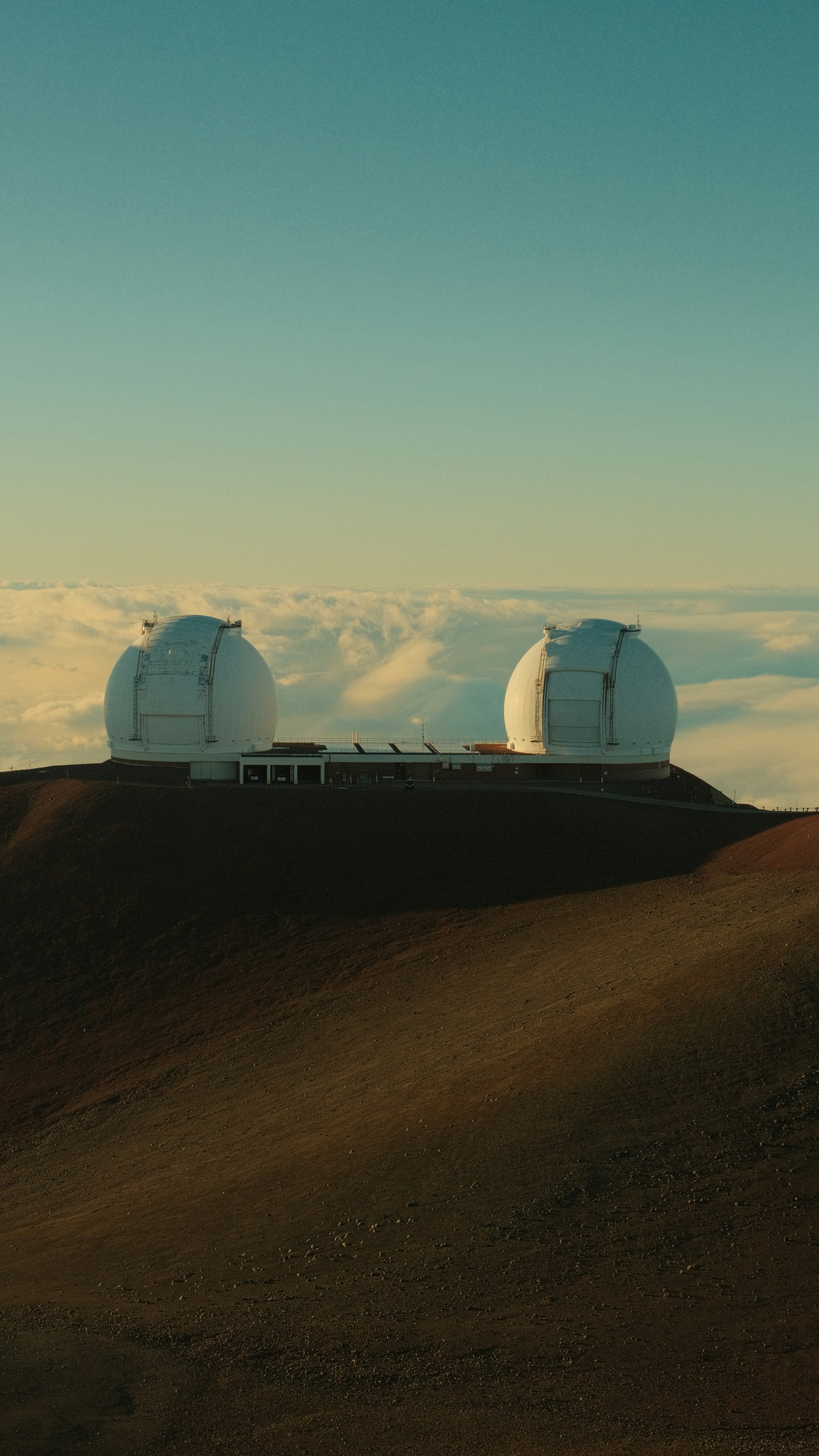 Two observatory domes on a volcanic summit above a sea of clouds